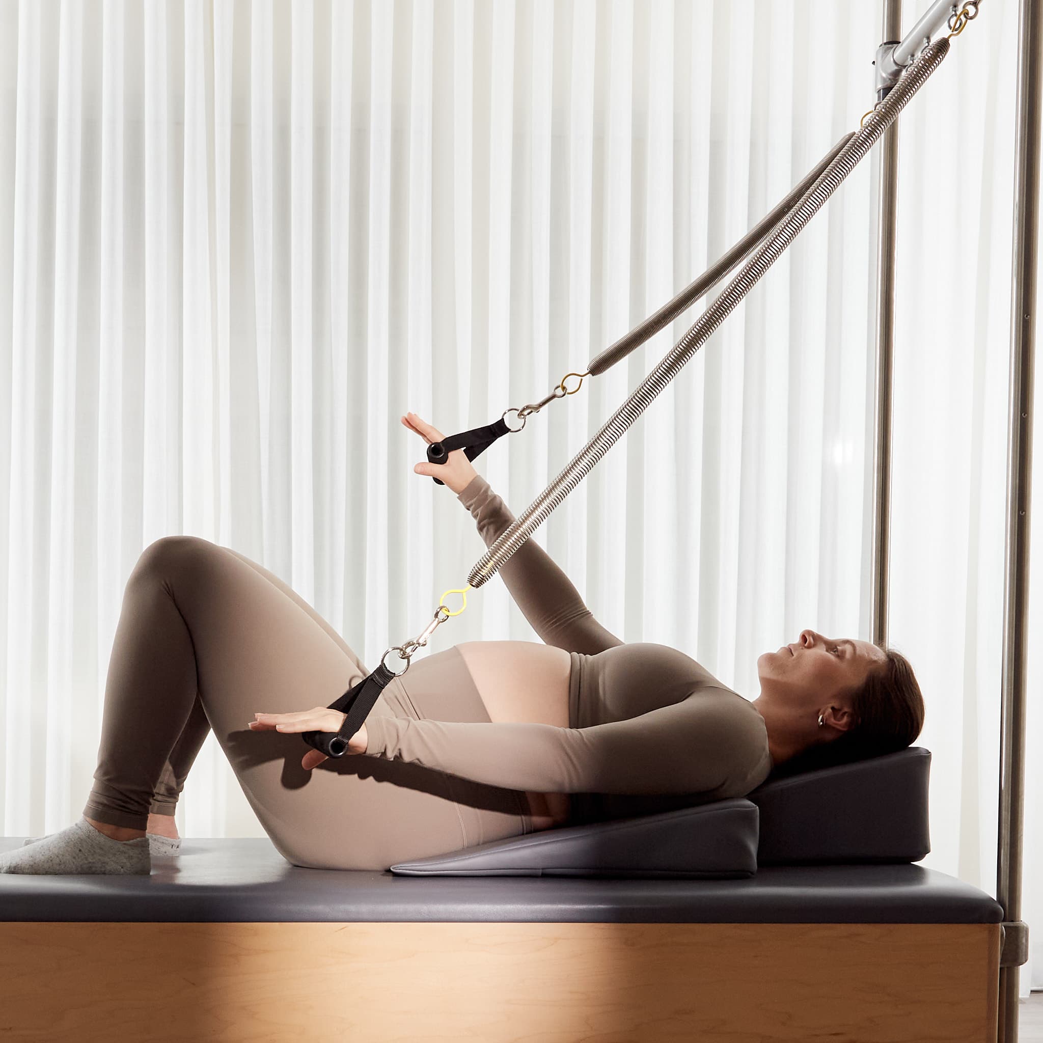 A pregnant client using the Cadillac arm springs with her upper body supported by a wedge